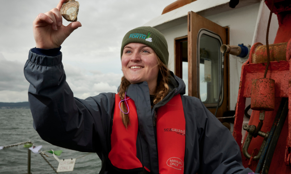 Emmy smiling and holding up a native oyster into the air.