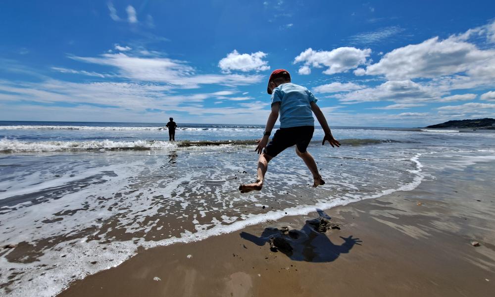 A young boy jumps in the shallow waves on a day at the beach