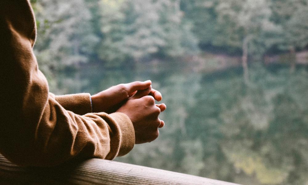 Arms resting on wooden fence over overlooking lake