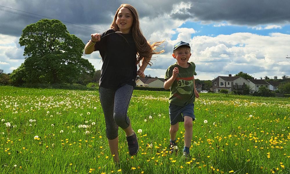 Two kids running in field opposite some houses
