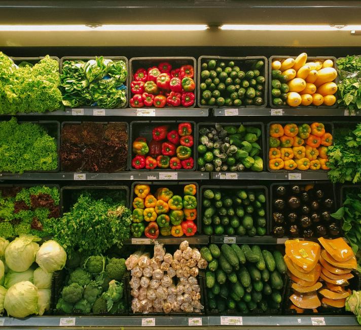 Photo of vegetables on shelves for sale at a market or supermarket including lettuce, red, yellow and green peppers and cucumbers