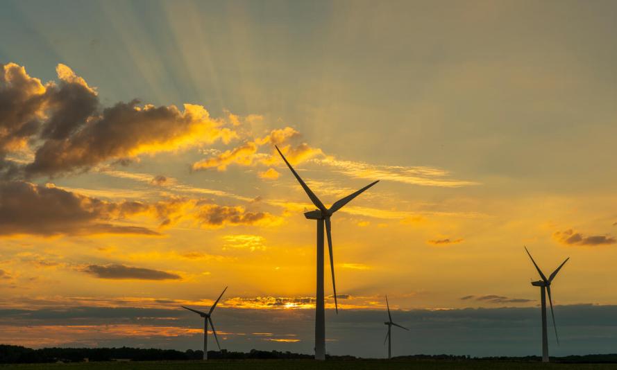 Wind turbines are backlit by the setting sun in Norfolk, UK.