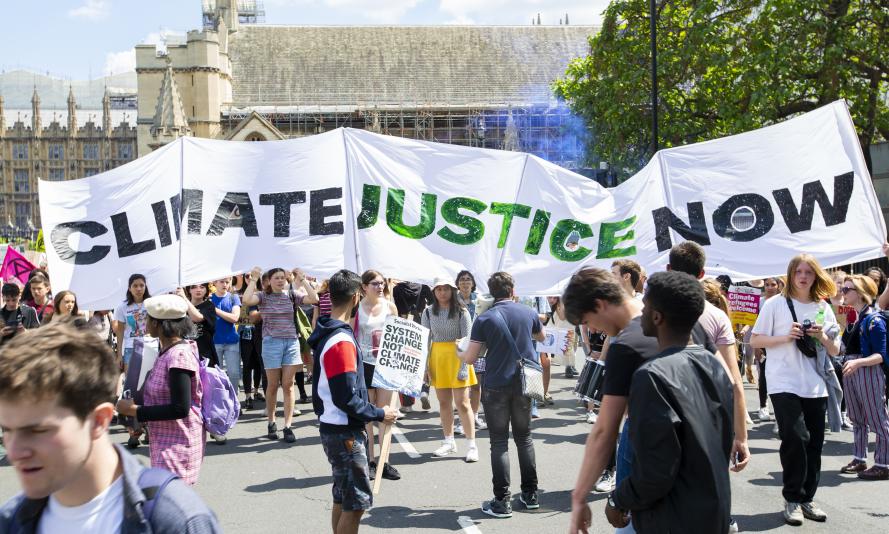 Large white banner on a march reading "climate justice now" in green and brown letters