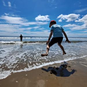 A young boy jumps in the shallow waves on a day at the beach